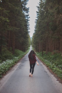 20-25 yaşlarındaki esmer, siyah taytlı ve ekose gömlekli bir kadın orman ortamında dans ediyor. Hareket ve temiz havanın keyfi. Orman Perisi.