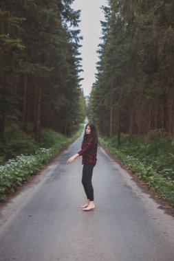 20-25 yaşlarındaki esmer, siyah taytlı ve ekose gömlekli bir kadın orman ortamında dans ediyor. Hareket ve temiz havanın keyfi. Orman Perisi.