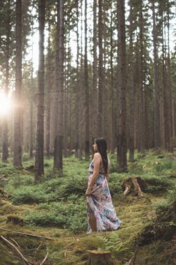 20-25 yaşlarındaki güzel esmer kız renkli bir elbiseyle ormanda dans ediyor. Temiz havanın neşesi ve doğanın gücü. Orman Perisi.