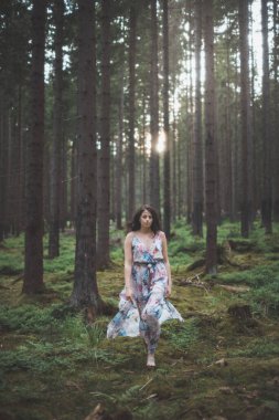 20-25 yaşlarındaki güzel esmer kız renkli bir elbiseyle ormanda koşuşturuyor. Temiz havanın neşesi ve doğanın gücü. Orman Perisi.