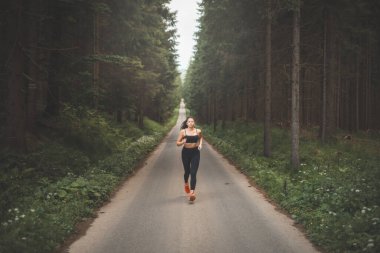 Esmer, 20-25 yaşlarında, siyah spor giyimli, akşam güneşinde doğada koşan. Aktif yaşam tarzı. Açık hava sporu.