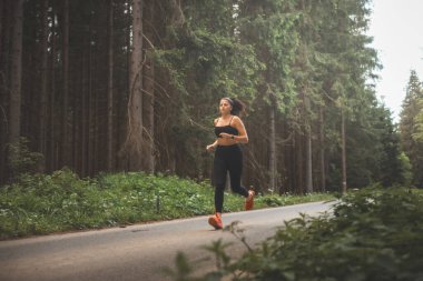 Esmer, 20-25 yaşlarında, siyah spor giyimli, akşam güneşinde doğada koşan. Aktif yaşam tarzı. Açık hava sporu.