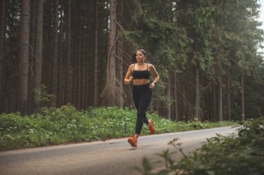 Esmer, 20-25 yaşlarında, siyah spor giyimli, akşam güneşinde doğada koşan. Aktif yaşam tarzı. Açık hava sporu.