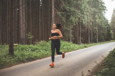 Esmer, 20-25 yaşlarında, siyah spor giyimli, akşam güneşinde doğada koşan. Aktif yaşam tarzı. Açık hava sporu.