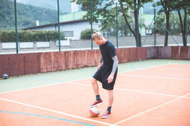 Güneşli bir günde, turuncu sahada topuyla hokkabazlık yapan genç bir adam. Spor kıyafetleri giyerek, topu doğal bir ortamda hassas bir şekilde kontrol etmeye odaklanıyor.