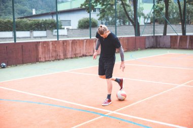 Güneşli bir günde, turuncu sahada topuyla hokkabazlık yapan genç bir adam. Spor kıyafetleri giyerek, topu doğal bir ortamda hassas bir şekilde kontrol etmeye odaklanıyor.