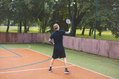 Badminton oyuncusu açık hava sahasında oynanan bir maçta havadaki pipiye odaklanıyor. Raketi yükselirken, kentsel ve manzaralı bir arka planla çevrili bir sonraki çekim için hazırlanıyor..