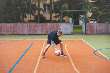 Basketbolcu, sahanın dışında oynanan sıradan bir maçta topu kontrol ediyor ve top sürüyor, odak noktasına eğiliyor. Saray ağaçlar ve doğa ile çevrili. Huzurlu ve atletik bir atmosfer sağlıyor..