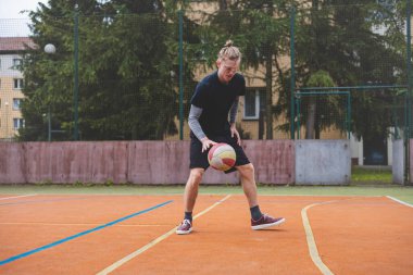 Basketbolcu, sahanın dışında oynanan sıradan bir maçta topu kontrol ediyor ve top sürüyor, odak noktasına eğiliyor. Saray ağaçlar ve doğa ile çevrili. Huzurlu ve atletik bir atmosfer sağlıyor..