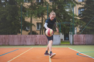 Basketbolcu, sahanın dışında oynanan sıradan bir maçta topu kontrol ediyor ve top sürüyor, odak noktasına eğiliyor. Saray ağaçlar ve doğa ile çevrili. Huzurlu ve atletik bir atmosfer sağlıyor..