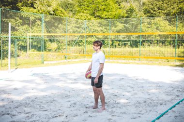 Genç adam voleybol sahasında elinde voleybol topuyla harekete hazır bekliyor. Sahne, güneşli bir günde oynanan açık hava maçı sırasında gelişigüzel ama odaklanmış bir anı yakalıyor..