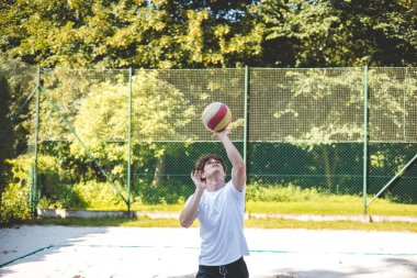 Genç adam, tek eliyle voleybol oynuyor. Açık havada bir antrenman sırasında. Sahne, güneşli, yeşil bir ortamda odak ve beceri gelişimi yakalıyor..