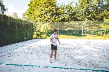 Genç adam, tek eliyle voleybol oynuyor. Açık havada bir antrenman sırasında. Sahne, güneşli, yeşil bir ortamda odak ve beceri gelişimi yakalıyor..