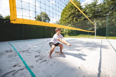 Genç adam hazır durumda, voleybol topu almaya ya da kazmaya hazırlanıyor. Sahil voleybolunun yoğunluğunu ve odak noktasını açık hava ortamında yakalamak.
