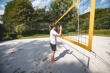 Bir voleybolu engellemek için atlayan genç bir adamın kum sahası üzerinden arka plan görüntüsü. Açık hava sahnesi yaz sporlarının ve plaj voleybolunun yoğunluğunu yakalıyor..
