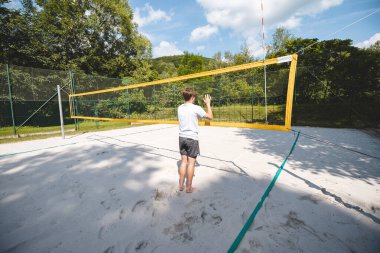 Bir voleybolu engellemek için atlayan genç bir adamın kum sahası üzerinden arka plan görüntüsü. Açık hava sahnesi yaz sporlarının ve plaj voleybolunun yoğunluğunu yakalıyor..