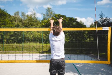 Voleybol oyuncusu voleybolu engellemek için atlıyor. Açık hava sahnesi yaz sporlarının ve plaj voleybolunun yoğunluğunu yakalıyor..