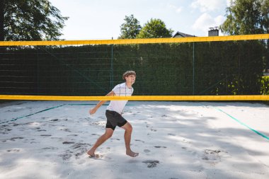 Voleybol oyuncusu voleybolu engellemek için atlıyor. Açık hava sahnesi yaz sporlarının ve plaj voleybolunun yoğunluğunu yakalıyor..