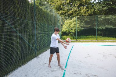 Voleybol oyuncusu kumda pas pratiği yapıyor, teknik ve kontrole odaklanıyor. Sahilde bir voleybol sahasında yakalanmış..