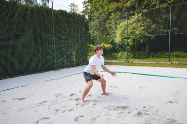 Genç adam hazır durumda, voleybol topu almaya ya da kazmaya hazırlanıyor. Sahil voleybolunun yoğunluğunu ve odak noktasını açık hava ortamında yakalamak.
