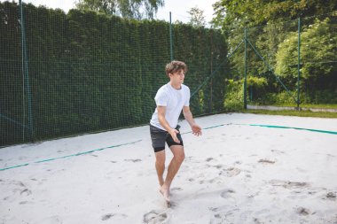 Genç adam hazır durumda, voleybol topu almaya ya da kazmaya hazırlanıyor. Sahil voleybolunun yoğunluğunu ve odak noktasını açık hava ortamında yakalamak.