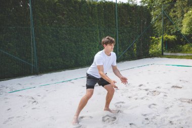 Genç adam hazır durumda, voleybol topu almaya ya da kazmaya hazırlanıyor. Sahil voleybolunun yoğunluğunu ve odak noktasını açık hava ortamında yakalamak.