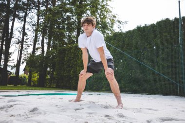 Genç adam hazır durumda, voleybol topu almaya ya da kazmaya hazırlanıyor. Sahil voleybolunun yoğunluğunu ve odak noktasını açık hava ortamında yakalamak.