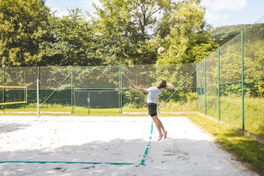 Voleybol oyuncusu, güneşli bir günde top oynamak için yükseğe zıpladı. Dinamik bir açık hava anı, atletizm gösterisi ve plaj voleyboluna odaklanma.