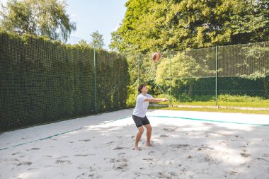Voleybol oyuncusu, top sahasında pas veriyor, hassas top kontrolü ve tekniğine odaklanıyor. Yoğun bir plaj voleybolu maçında yakalandı..