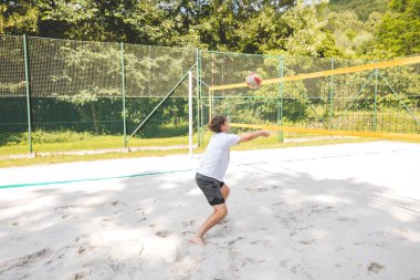 Voleybol oyuncusu, top sahasında pas veriyor, hassas top kontrolü ve tekniğine odaklanıyor. Yoğun bir plaj voleybolu maçında yakalandı..