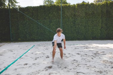 Voleybol oyuncusu topu bir kum sahasından alıyor ve sıradan bir plaj voleybolu maçına hazırlanıyor. Sakin bir ortamda yakalandılar..