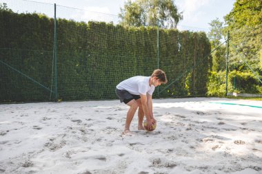 Voleybol oyuncusu topu bir kum sahasından alıyor ve sıradan bir plaj voleybolu maçına hazırlanıyor. Sakin bir ortamda yakalandılar..