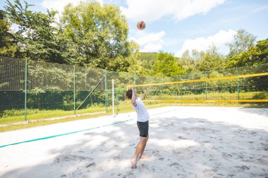 Voleybol oyuncusu bir açık hava maçı sırasında topu ağdan atmak için atlıyor. Eylem, plaj voleybolunun yoğunluğunu ve atletizmini yakalıyor..