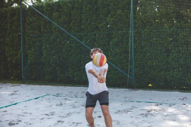 Voleybol oyuncusu, voleybol topunu kumlu bir sahada kazıyor. Sahil voleybolunun yoğunluğunu ve odak noktasını açık hava ortamında yakalamak.