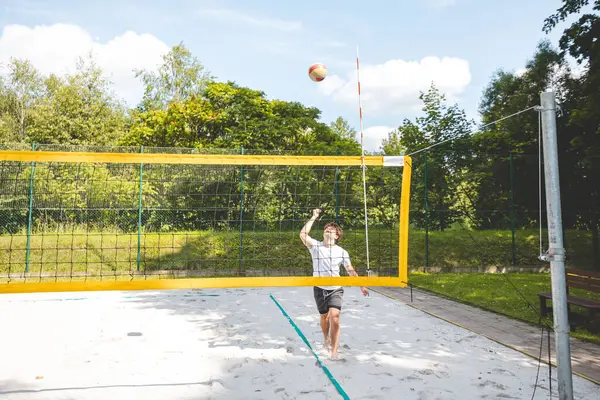 Voleybol oyuncusu bir açık hava maçı sırasında topu ağdan atmak için atlıyor. Eylem, plaj voleybolunun yoğunluğunu ve atletizmini yakalıyor..