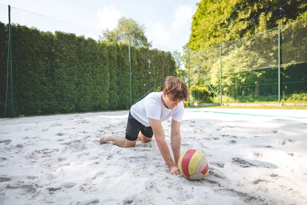 Voleybol oyuncusu, voleybol topunu kumlu bir sahada kazıyor. Sahil voleybolunun yoğunluğunu ve odak noktasını açık hava ortamında yakalamak.