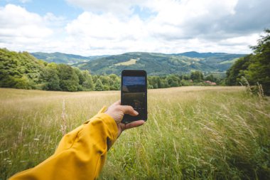 Akıllı bir telefonla Beskydy Dağları 'ndaki yuvarlanan tarlaların ve yeşil ormanların resimli manzarasını yakalar ve modern teknolojiyi doğal güzellikle harmanlar..