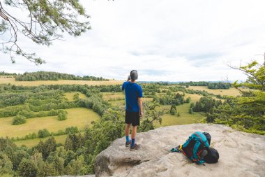 Mavi tişörtlü ve şapkalı genç, geniş yeşil tarlalara ve Beskydy Dağları 'nın yuvarlanan tepelerine bakarken bir su şişesinden ferahlatıcı bir içecek içiyor..