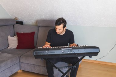 young man playing a digital keyboard in a cozy living room with a minimalist design. The relaxed atmosphere emphasizes focus and a passion for music. clipart