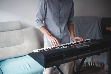 Müzisyenin elleri aktif olarak dijital bir klavye çalıyor, modern bir ev ortamındaki odak ve yaratıcılığı hafif ışıklandırma ve minimalist dekorla harmanlıyor.