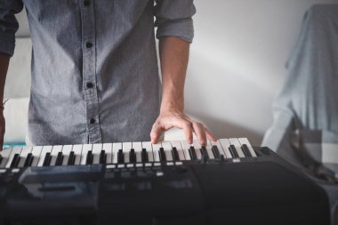 Müzisyenin elleri aktif olarak dijital bir klavye çalıyor, modern bir ev ortamındaki odak ve yaratıcılığı hafif ışıklandırma ve minimalist dekorla harmanlıyor.