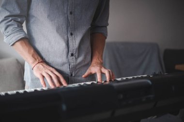 Müzisyenin elleri aktif olarak dijital bir klavye çalıyor, modern bir ev ortamındaki odak ve yaratıcılığı hafif ışıklandırma ve minimalist dekorla harmanlıyor.