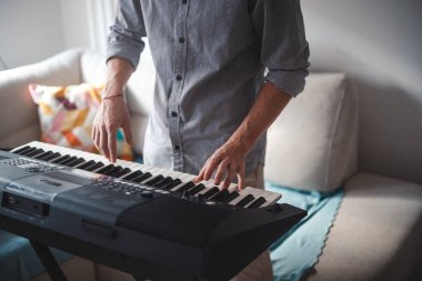 Müzisyenin elleri aktif olarak dijital bir klavye çalıyor, modern bir ev ortamındaki odak ve yaratıcılığı hafif ışıklandırma ve minimalist dekorla harmanlıyor.