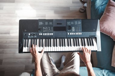 Sıcak doğal ışık altında dijital bir klavye çalan ellerin yakın çekimi, yaratıcılığın, odaklanmanın ve kapalı bir ortamda müzik tutkusunun özünü yakalıyor..