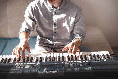 Sıcak doğal ışık altında dijital bir klavye çalan ellerin yakın çekimi, yaratıcılığın, odaklanmanın ve kapalı bir ortamda müzik tutkusunun özünü yakalıyor..