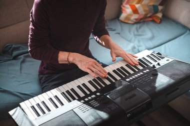 Güneşli bir odada dijital klavye çalan bir insanın genel görünümü, yumuşak doğal ışık ve rahat bir atmosferle bir odak ve yaratıcılık anını vurguluyor. Müzik hayatı.