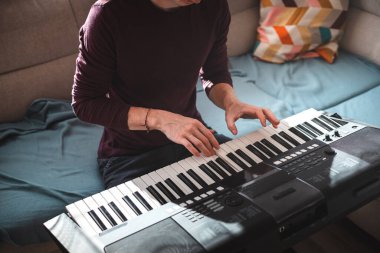 Güneşli bir odada dijital klavye çalan bir insanın genel görünümü, yumuşak doğal ışık ve rahat bir atmosferle bir odak ve yaratıcılık anını vurguluyor. Müzik hayatı.
