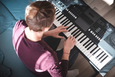 Güneşli bir odada dijital klavye çalan bir insanın genel görünümü, yumuşak doğal ışık ve rahat bir atmosferle bir odak ve yaratıcılık anını vurguluyor. Müzik hayatı.
