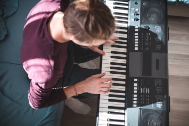 Güneşli bir odada dijital klavye çalan bir insanın genel görünümü, yumuşak doğal ışık ve rahat bir atmosferle bir odak ve yaratıcılık anını vurguluyor. Müzik hayatı.