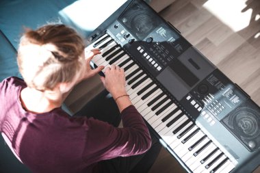 Güneşli bir odada dijital klavye çalan bir insanın genel görünümü, yumuşak doğal ışık ve rahat bir atmosferle bir odak ve yaratıcılık anını vurguluyor. Müzik hayatı.